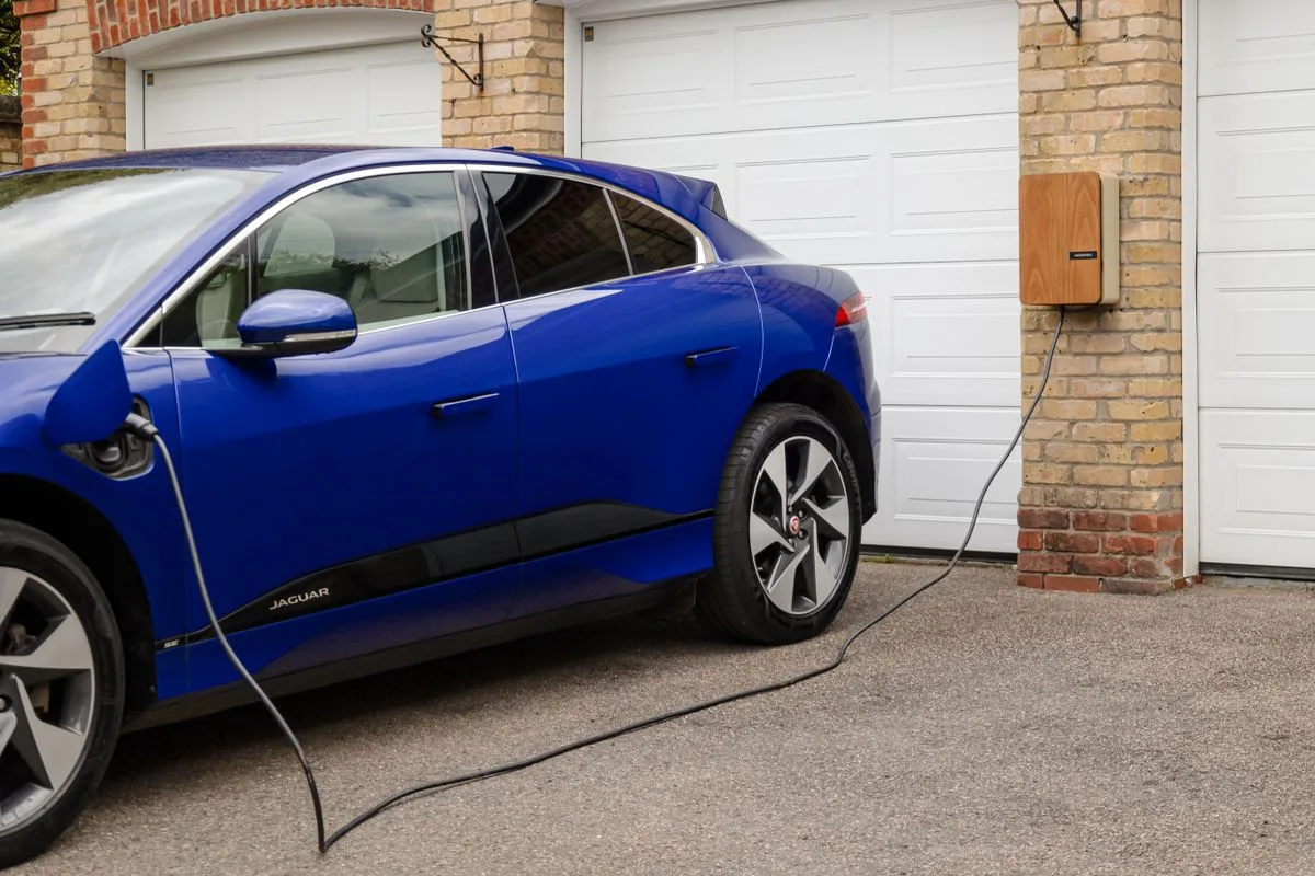 An der Hauswand montierte Wallbox lädt ein Elektroauto in der Garageneinfahrt